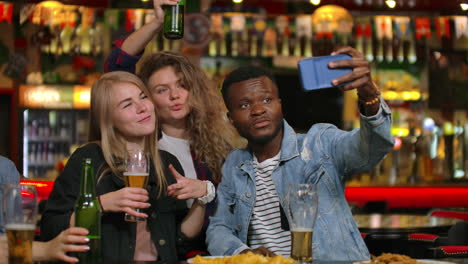 A-group-of-friends-multiethnic-resting-in-the-bar.-Friends-take-a-photo-on-the-phone-at-the-bar-make-a-shared-photo-on-the-phone.-Party-with-friends-at-the-bar-with-beer.